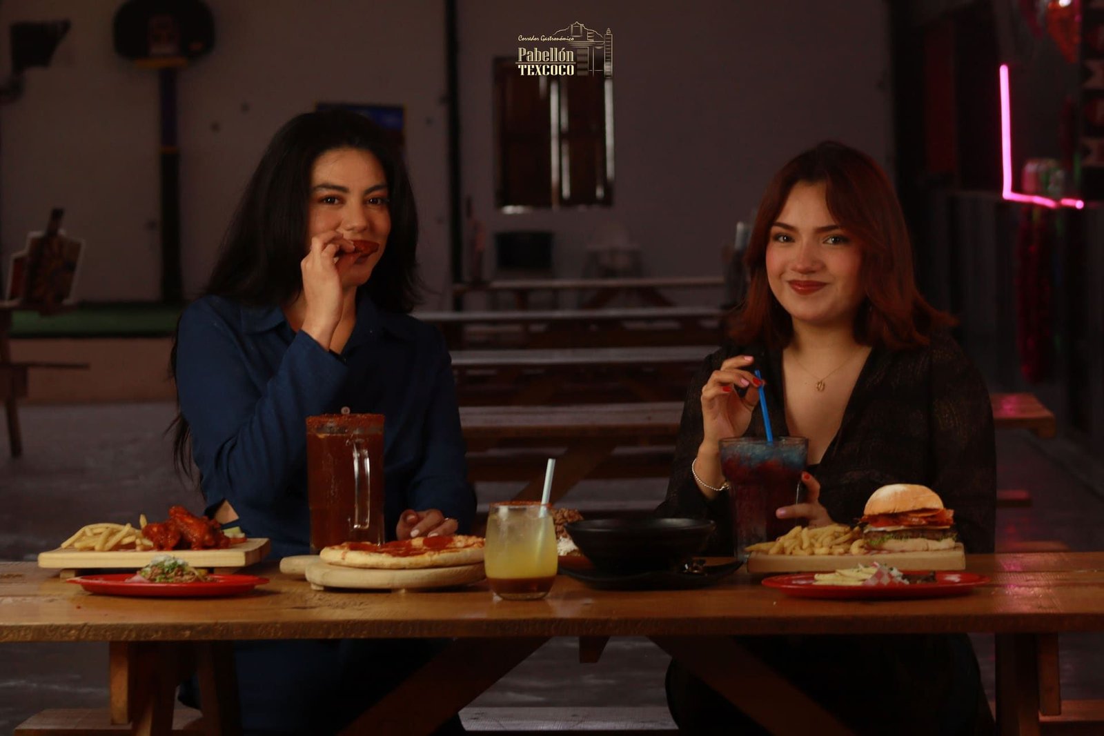 Mesa llena de platillos de Pabellón Texcoco: pizza, hamburguesa, alitas y bebidas